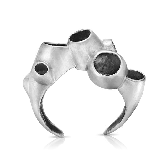 A sterling silver cuff bracelet with an oxidized interior and high polish rims, featuring an intricate, sea-inspired design with multiple openings that resemble marine structures.